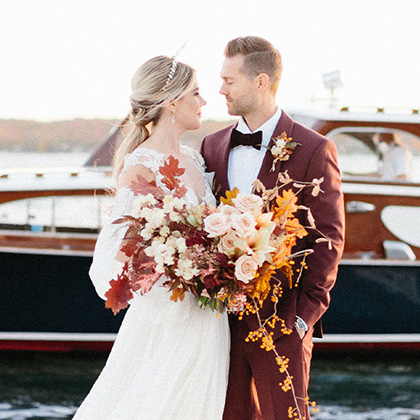 Bride and groom in a burgundy suit with an autumn bouquet by a vintage Lake Geneva wedding boat